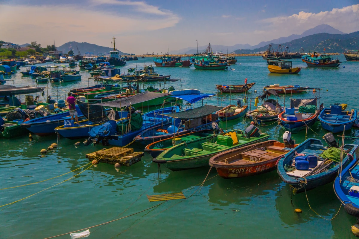 Colorful fishing boats moored on turquoise harbor water beneath hills in Hong Kong