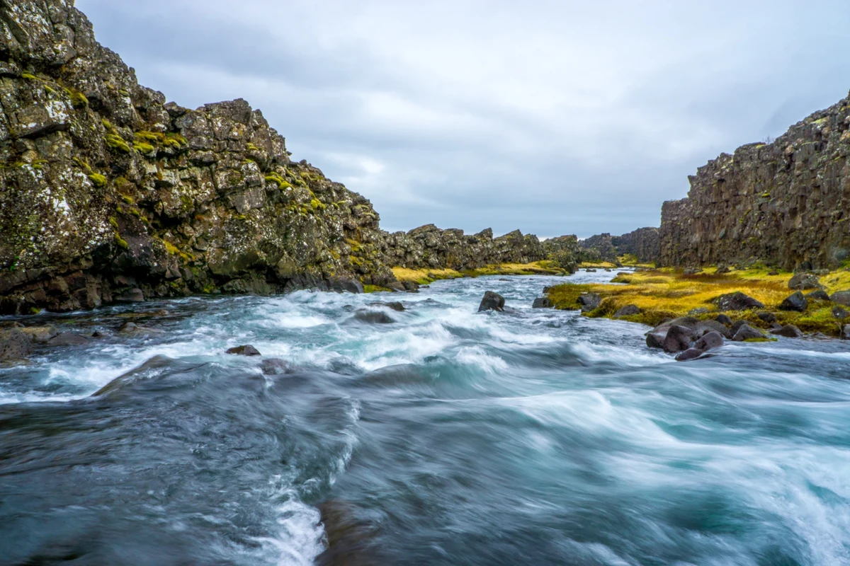 A rushing river between rugged rock walls and mossy banks in Iceland
