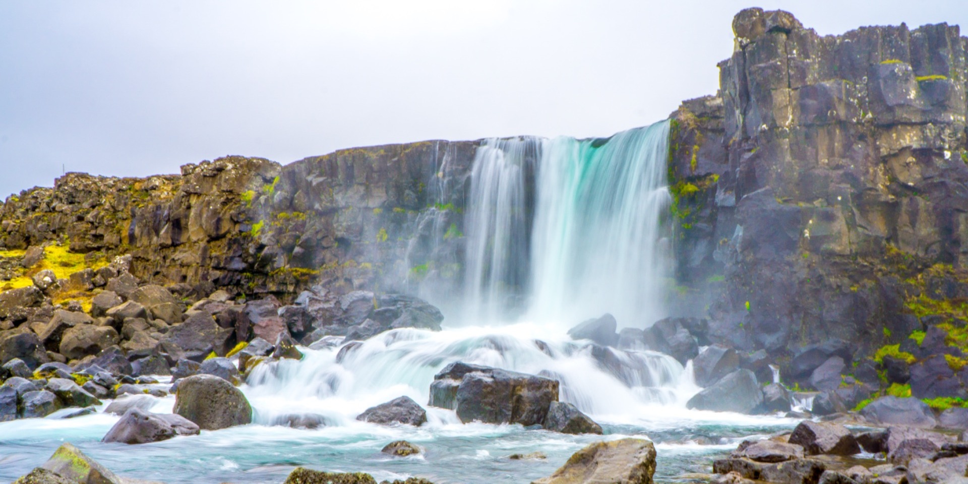 An Icelandic waterfall flowing over dark rock into a turquoise river